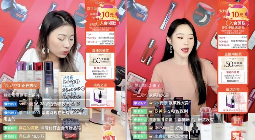 Duas moças chinesas estão apresentando live shoppings. Na imagem é possível ver vários produtos, como pergumes, garrafas e cosméticos que estão sendo apresentados.