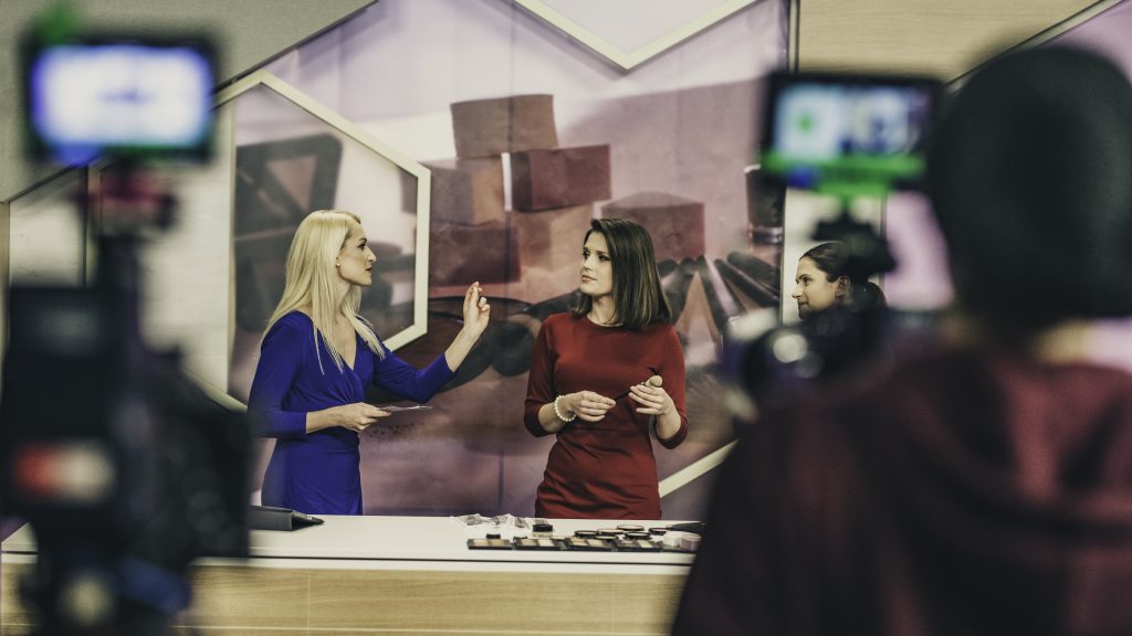 Nesta imagem podemos ver três apresentadoras em um estúdio de TV fazendo uma inserção de alguns produtos ao vivo, o que diz muito a respeito do que é merchan.