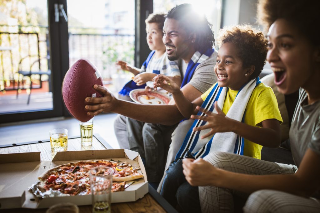 Nesta imagem podemos ver uma família assistindo a uma partida de futebol americano. Anunciar nos esportes é uma ótima oportunidade para implementar o marketing esportivo em sua estratégia de divulgação.
