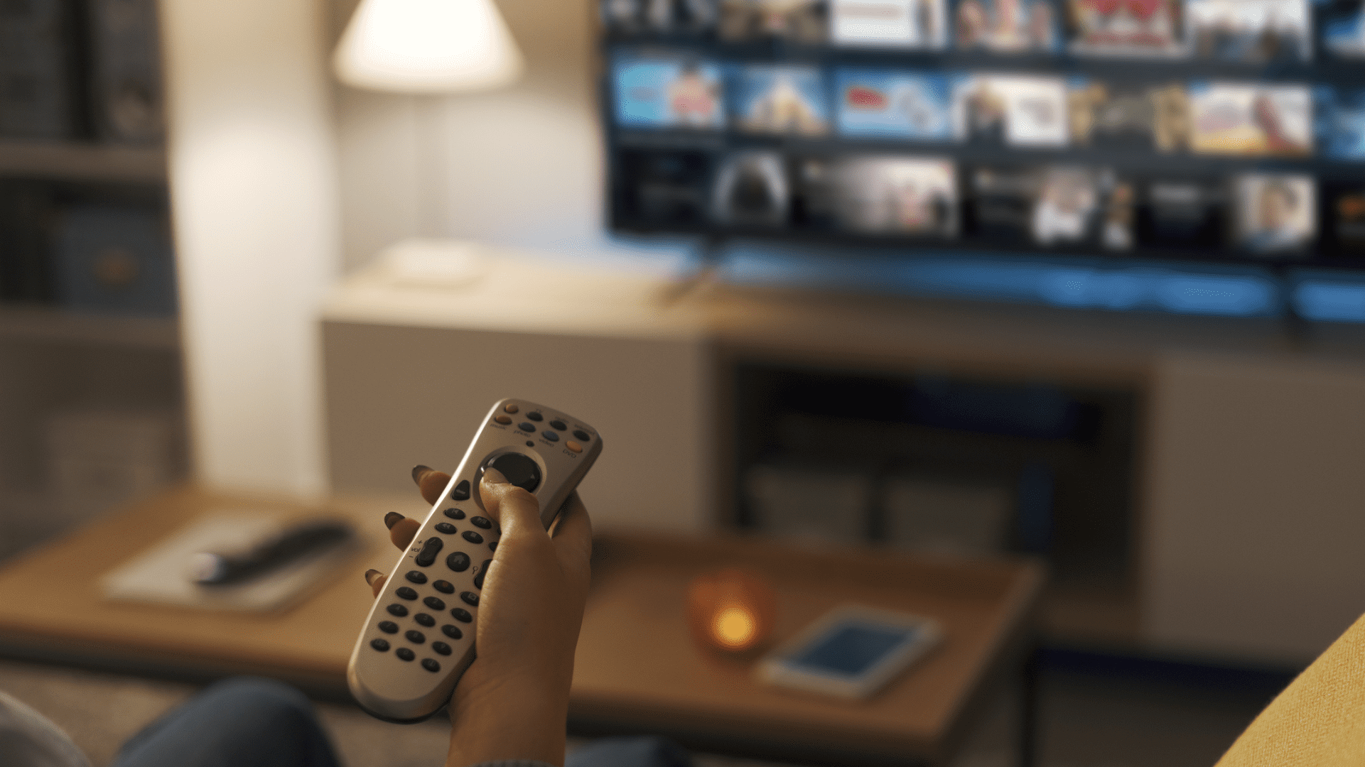 Nesta imagem podemos ver uma pessoa segurando um controle remoto enquanto assiste publicidade na TV aberta.