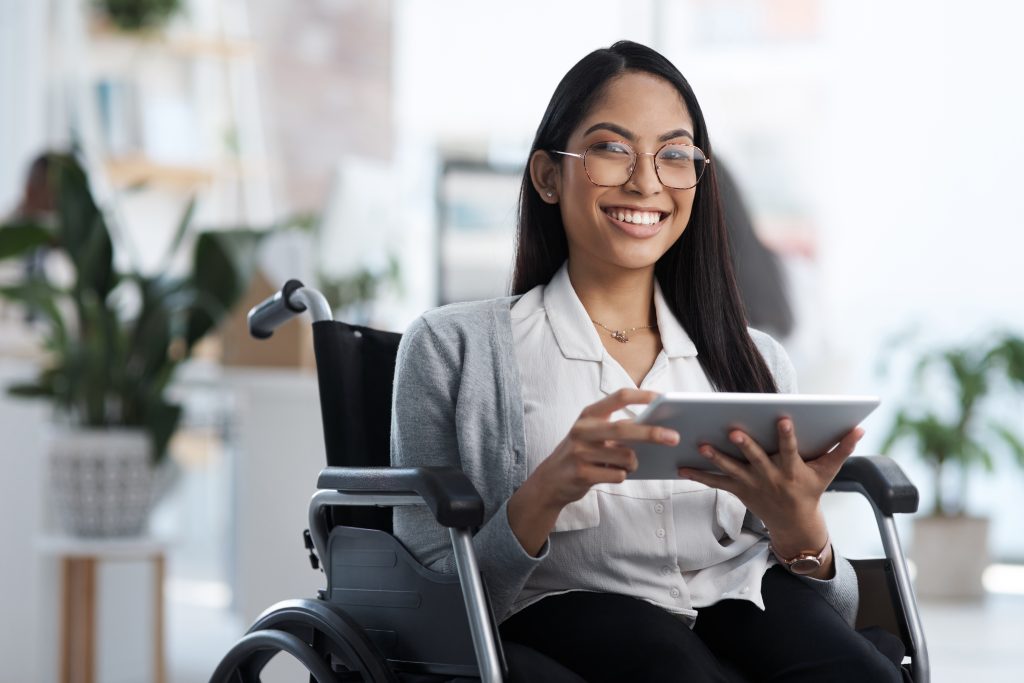 Pessoa com deficiência na cadeira de rodas segurando um tablet nas mãos, em busca de uma mídia mais inclusiva, nos lugares em que acessa.