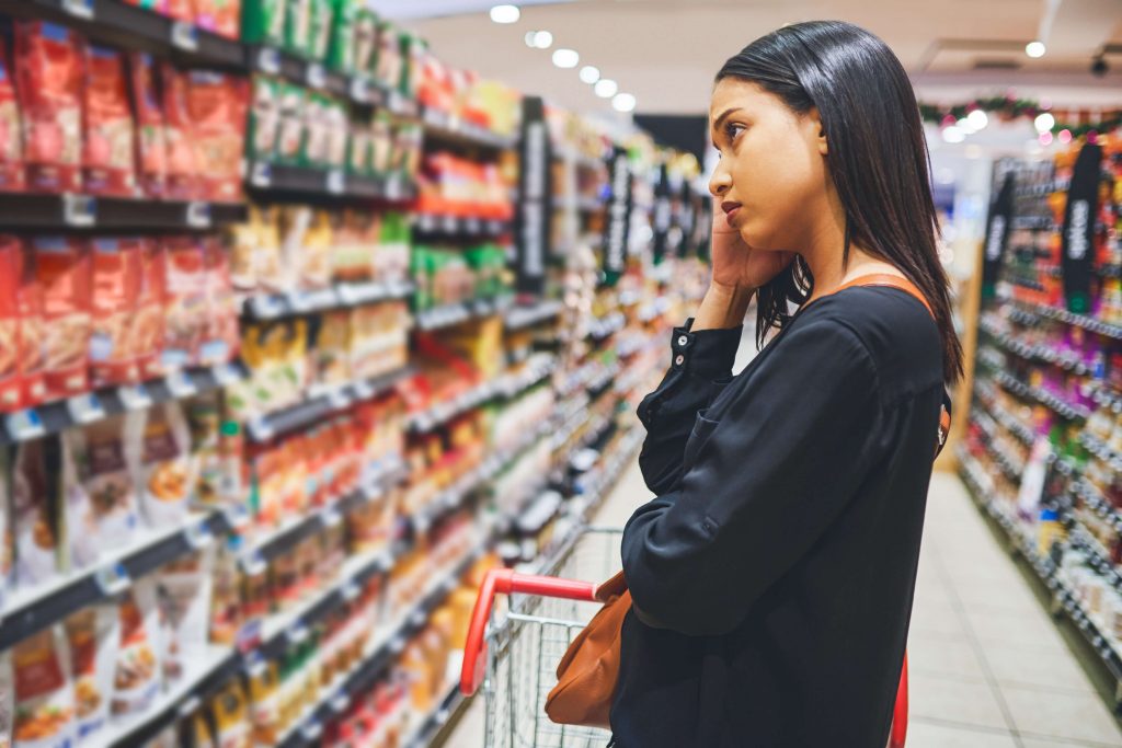 Nesta imagem podemos ver uma moça que parece estar pensativa quanto ao que comprar na Black Friday que está tendo em um supermercado.