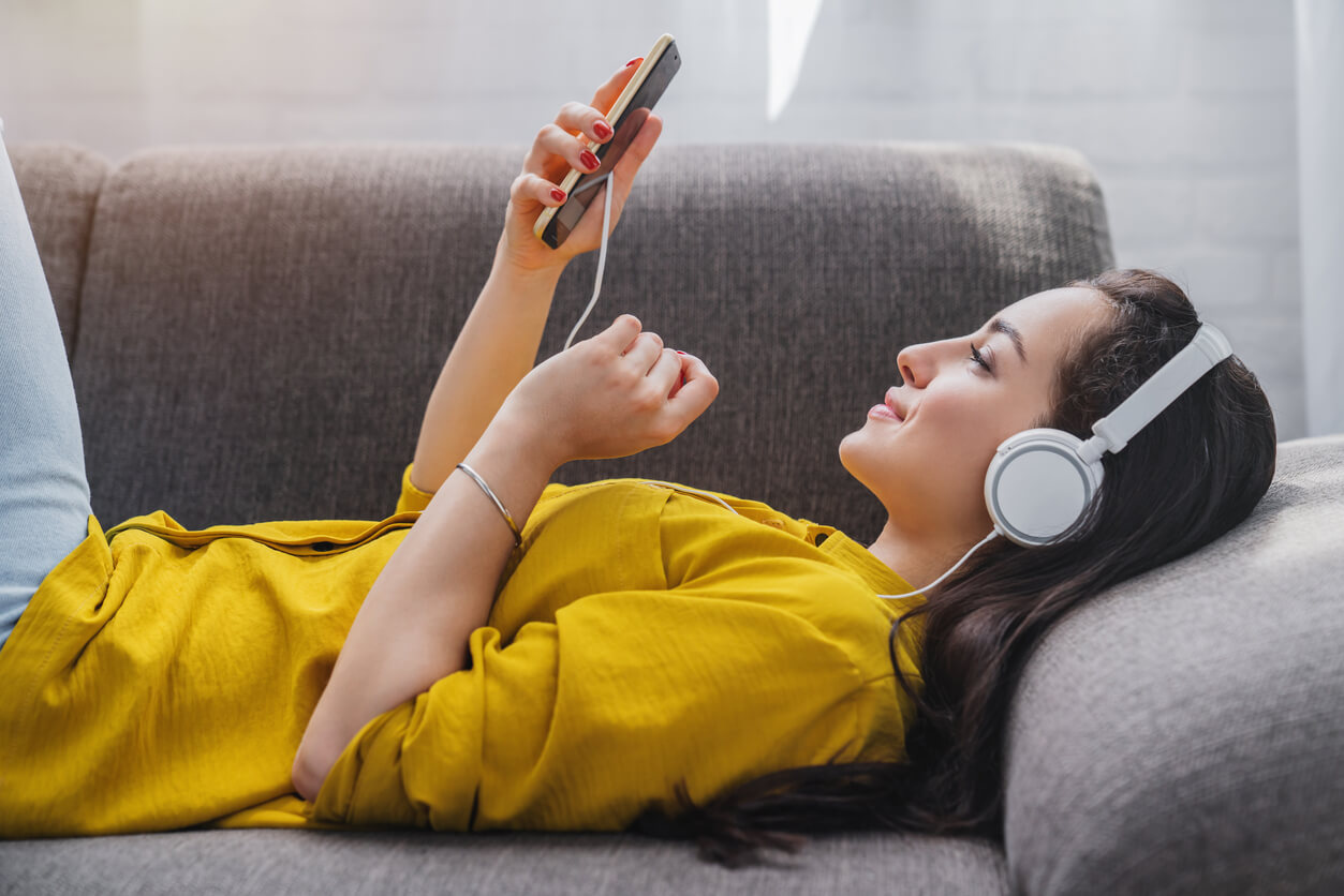 Mulher deitada no sofá ouvindo música no celular com fone de ouvido