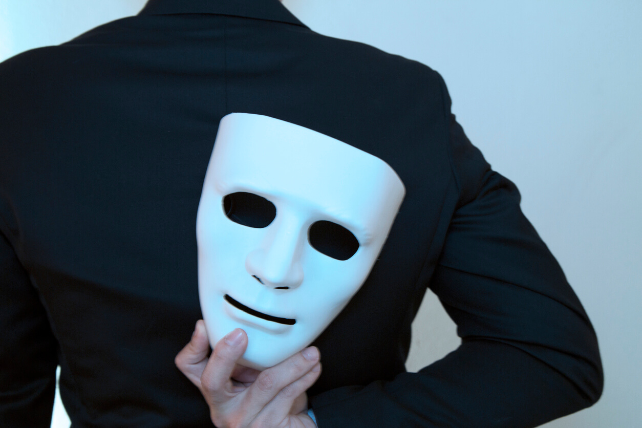 Homem usando terno preto de costas segurando uma máscara branca nas suas costas