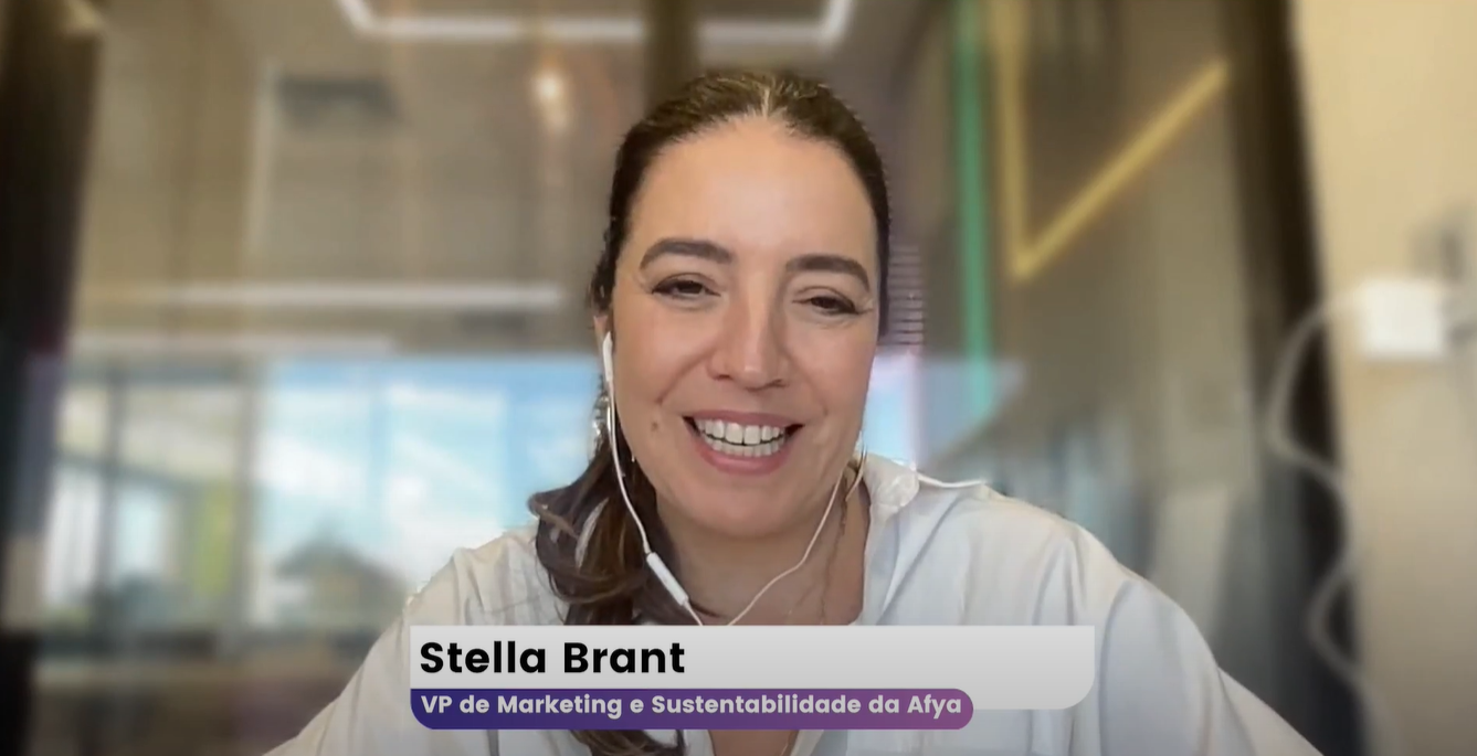 Stella Brant via reunião online sorrindo usando fone de ouvido com fio, ela está com o cabelo amarrado e usando camisa branca e fala sobre como criar marcas com propósito