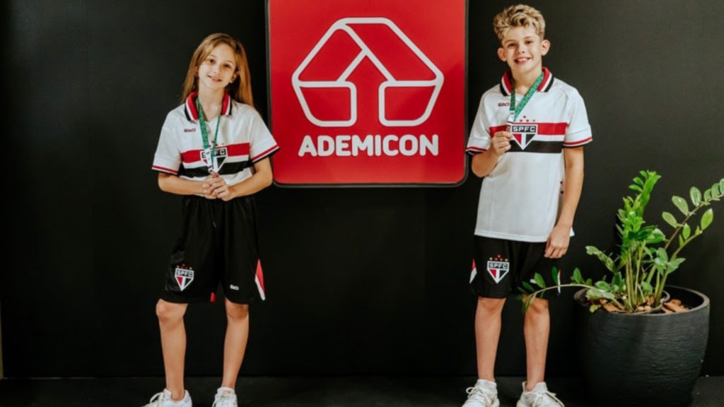 Um menino e uma menino estão caracterizados com o uniforme do São Paulo e trazem a corrente de autismo no pescoço.