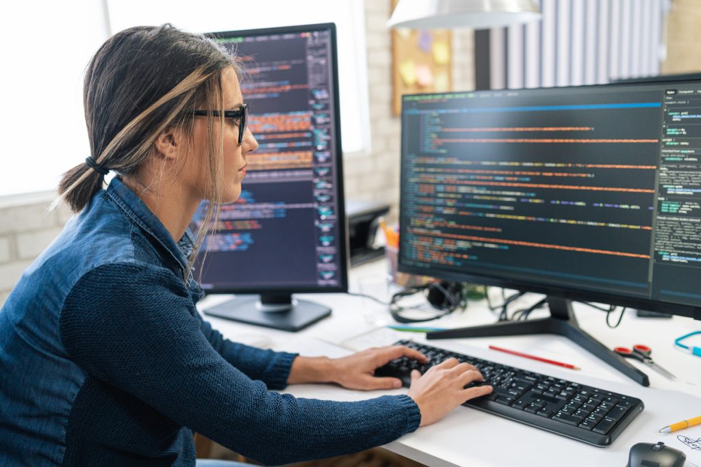Mulher branca de cabelos castanhos e óculos está olhando para a tela do computador.