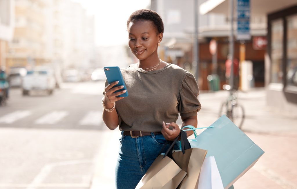 Foto de uma jovem atraente usando seu celular fora enquanto fazia compras na cidade para a Black Friday 2024.