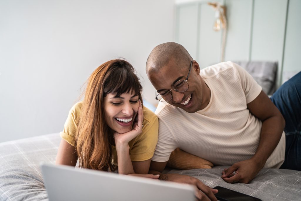 Jovem casal assistindo algo no laptop na cama em casa.