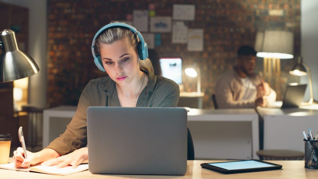 Fones de ouvido, noite e mulher de negócios escrevendo em um escritório de informática para prazos de artigo.