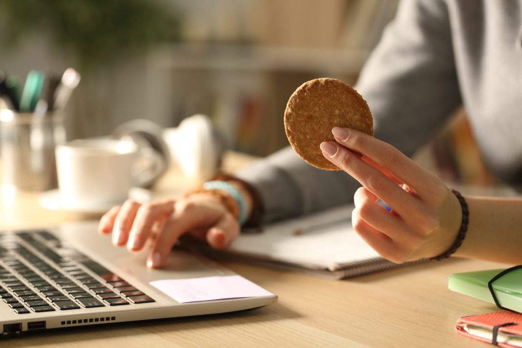 Aluno mãos segurando biscoito à noite estudando.