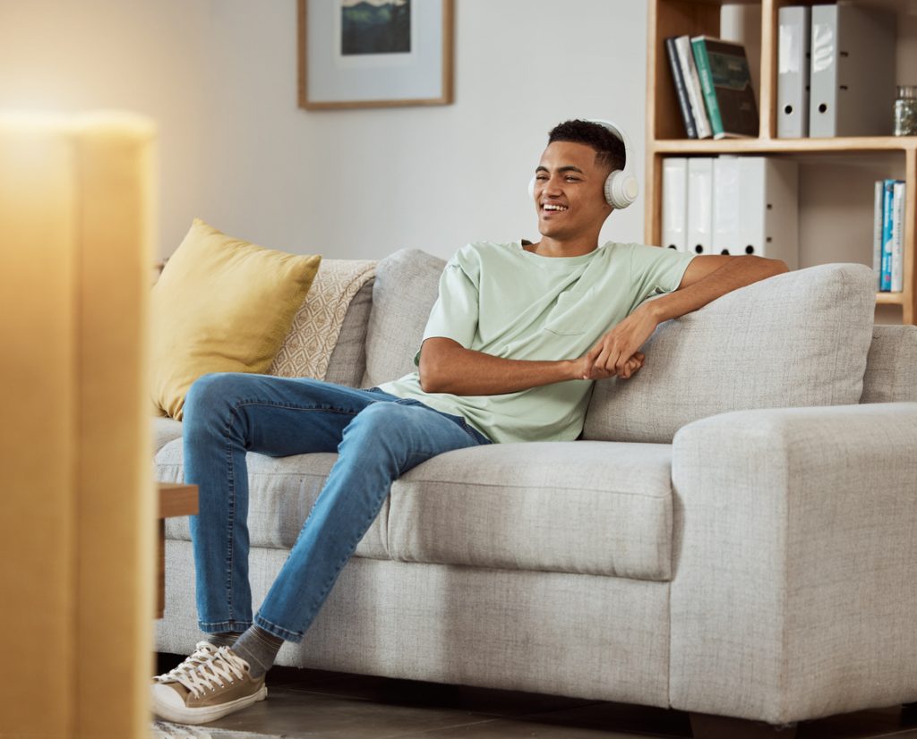 Fones de ouvido, assistindo tv e homem em um sofá da sala de estar feliz e relaxar em casa.