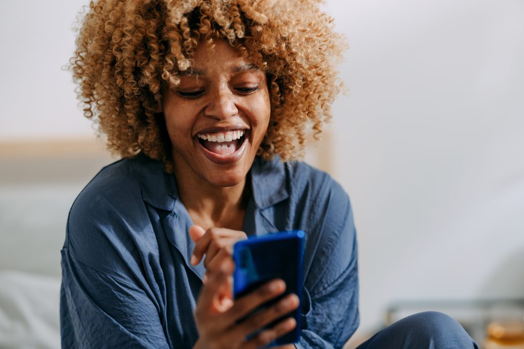 Mulher sorridente usando celular no quarto.