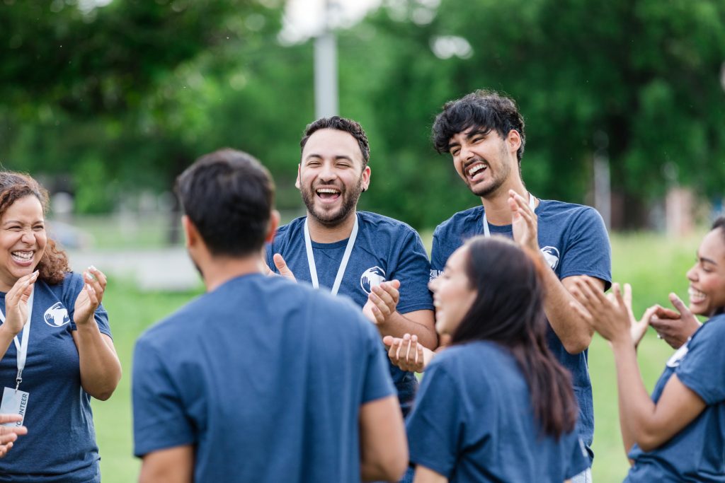 Grupo multirracial de voluntários sorri e bate palmas.