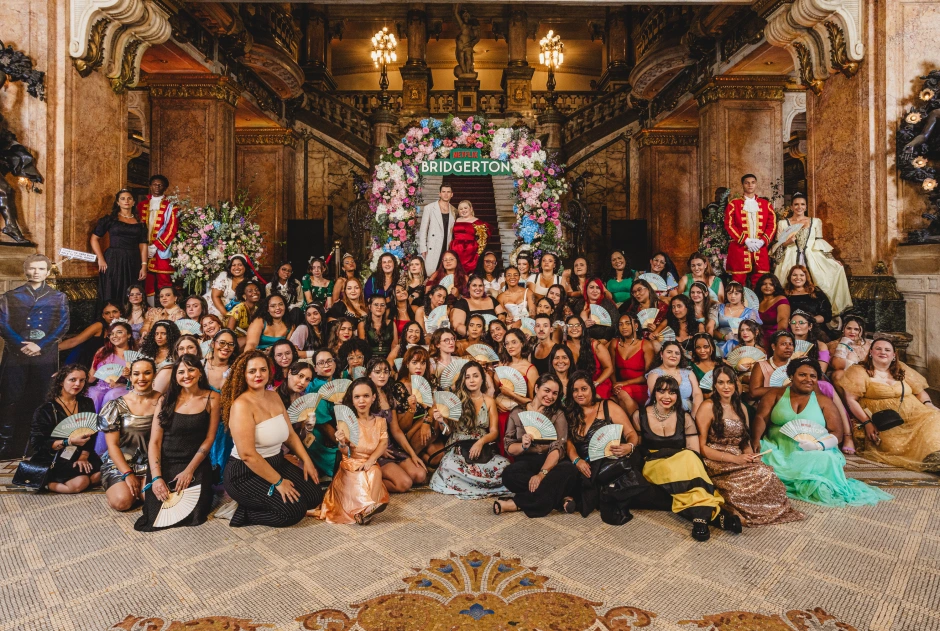 Fãs reunidas em uma foto em grupo. Elas usam vestidos da era regencial em um salão de baile funk trazendo experiências de marca.