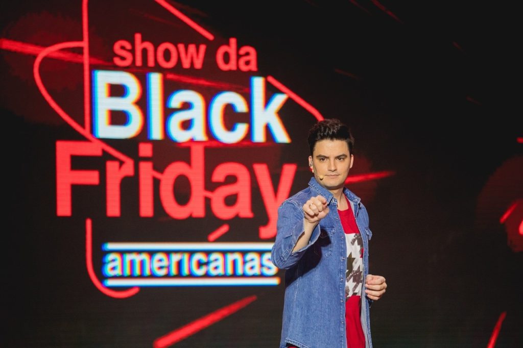 Felipe Neto em live shopping pela Americanas. Ele está em um palco e aponta o dedo indicador para frente.