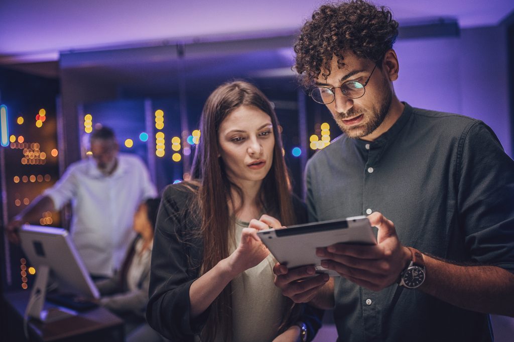 Um homem e uma mulher estão em um laboratório e seguram um tablet em conjunto, enquanto olham para ele com um olhar de quem analisa algo.