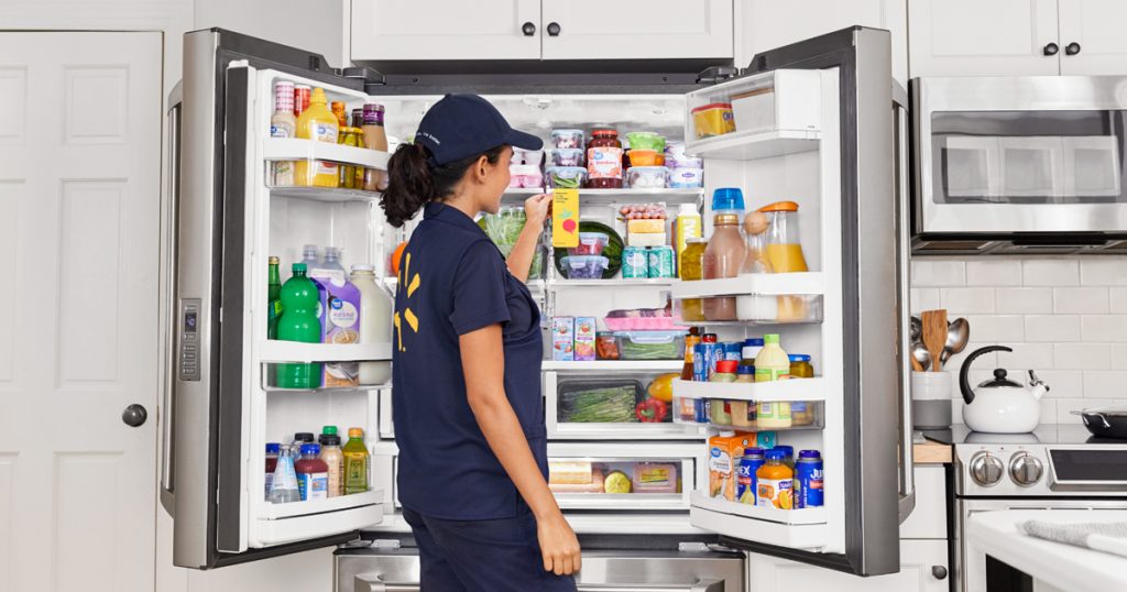 Mulher uniformizada com as roupas da Walmart arruma protudos de consumo alimentício em uma geladeira.