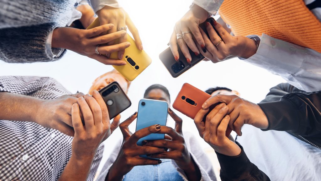 Adolescentes em círculo segurando telefones celulares inteligentes. Imagem: Reprodução/ iStock