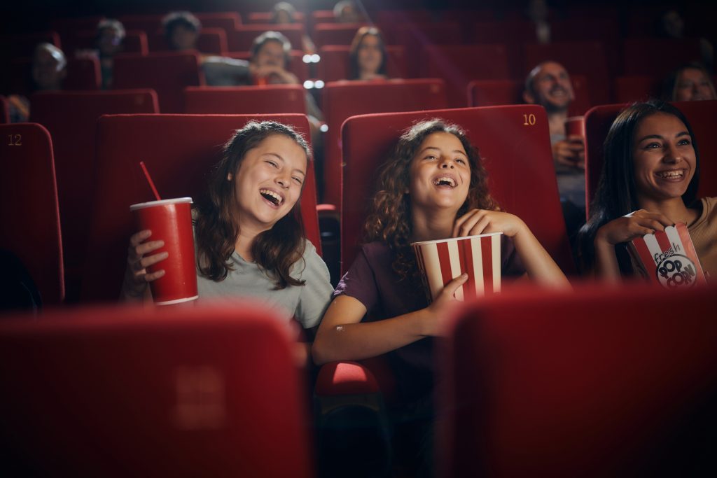 Amigas alegres assistindo filme no cinema. Muitas estratégias utilizadas no marketing cinematográfico se relacionam com as redes sociais.