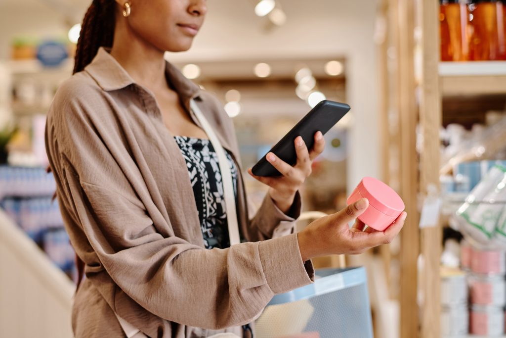 Mulher negra pega produto em pateleira de supermercado e scaneia o código de barras dele com o celular. Quando o consumidor já sabe o que quer e vai direto ao ponto, isso significa que a marca contruiu um bom brand equity.