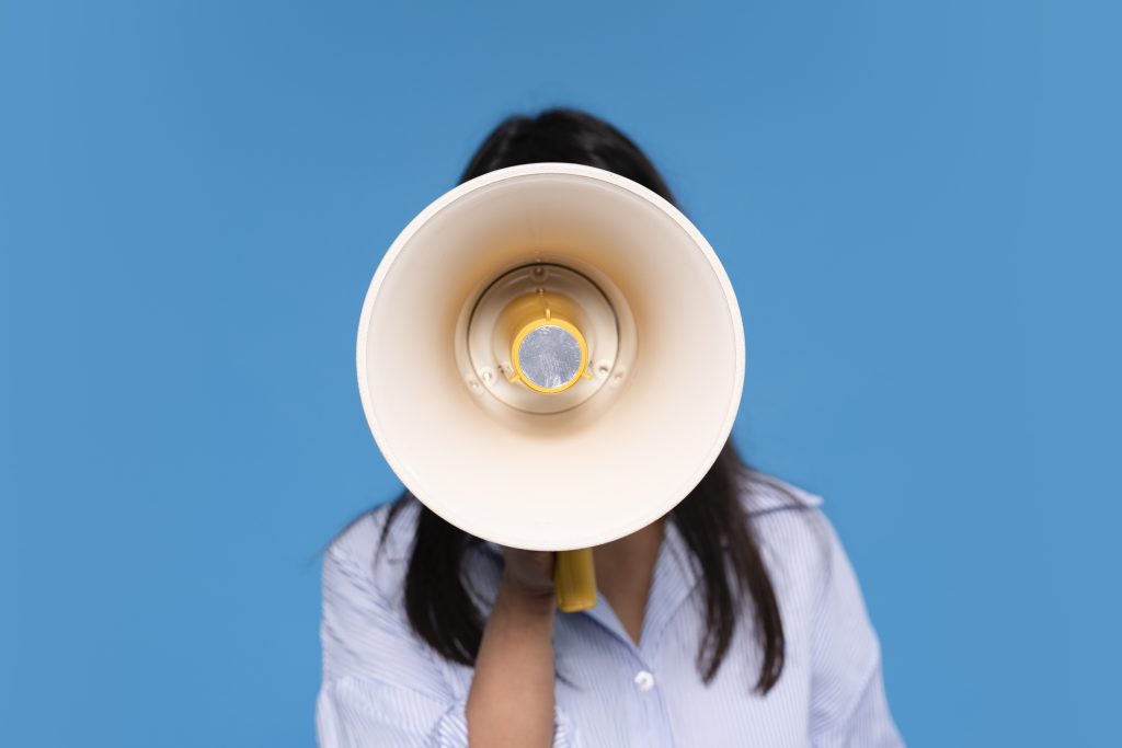 Mulher segurando megafone contra fundo azul sólido.