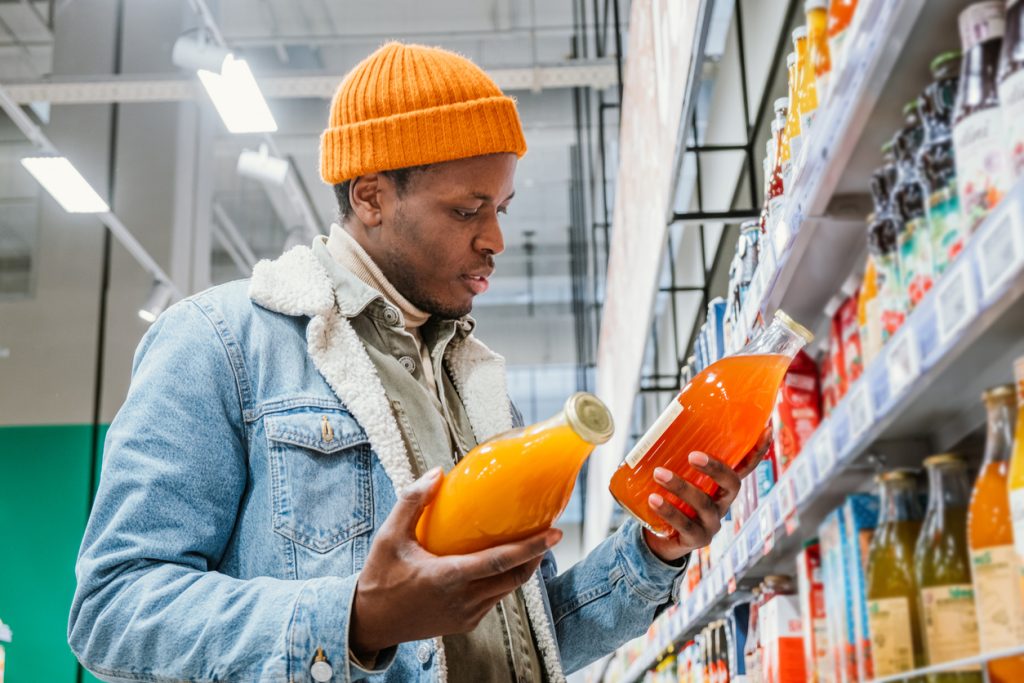 Homem africano escolhe suco natural em garrafas de vidro em supermercado