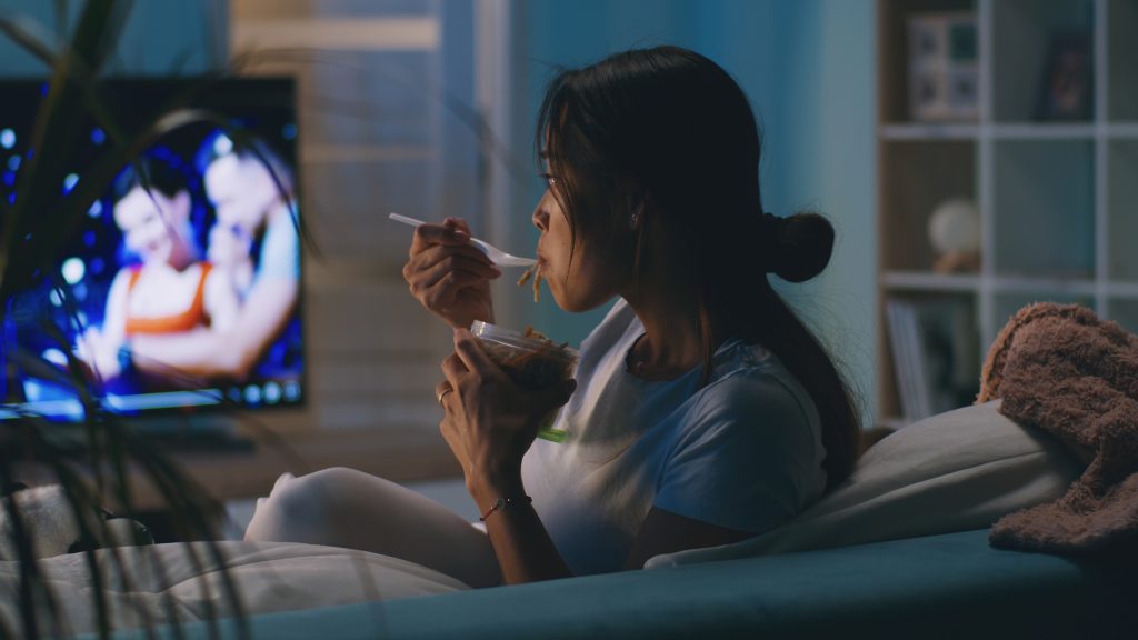 Mulher comendo na frente da TV.