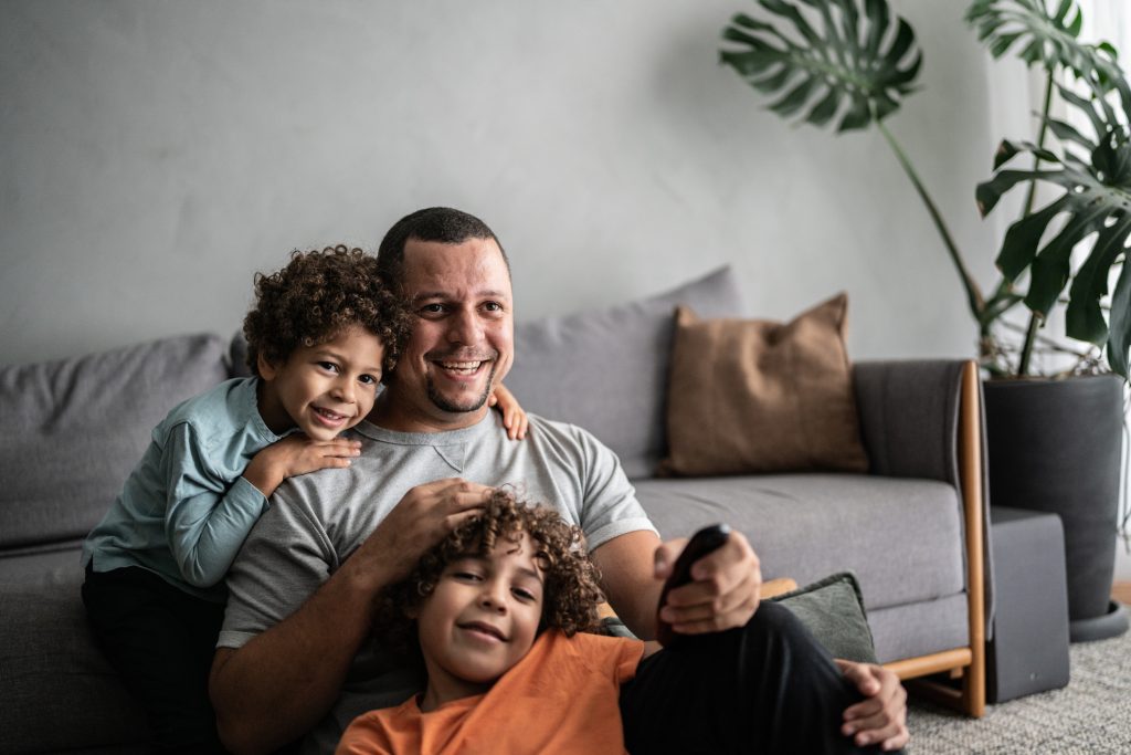 Pai e filhos assistindo TV em casa.