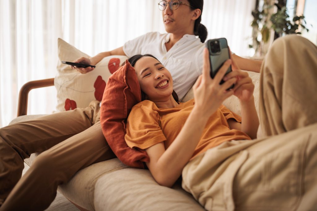 Casal deitado no sofá assistindo TV e mexendo no celular