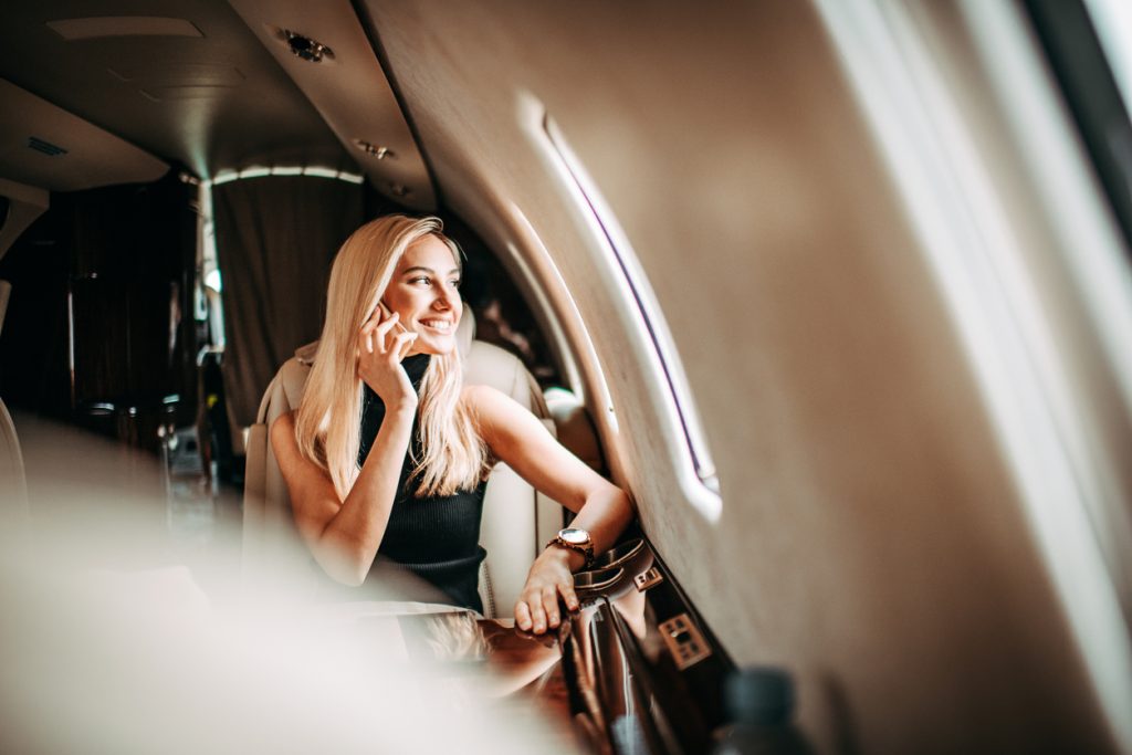 Jovem empresária falando sobre um telefone móvel enquanto viajava em um avião privado. Aviões a jato são imaginários do marketing de luxo.