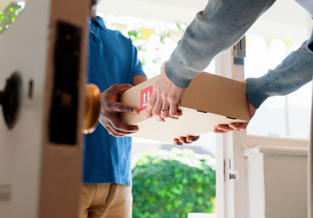 Mãos, caixa e entregador na porta de casa com cliente, serviços e envio para produto comercial. 