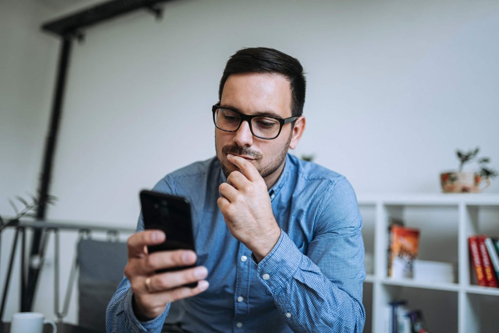 Homem pensativo novo que olha o telefone móvel.