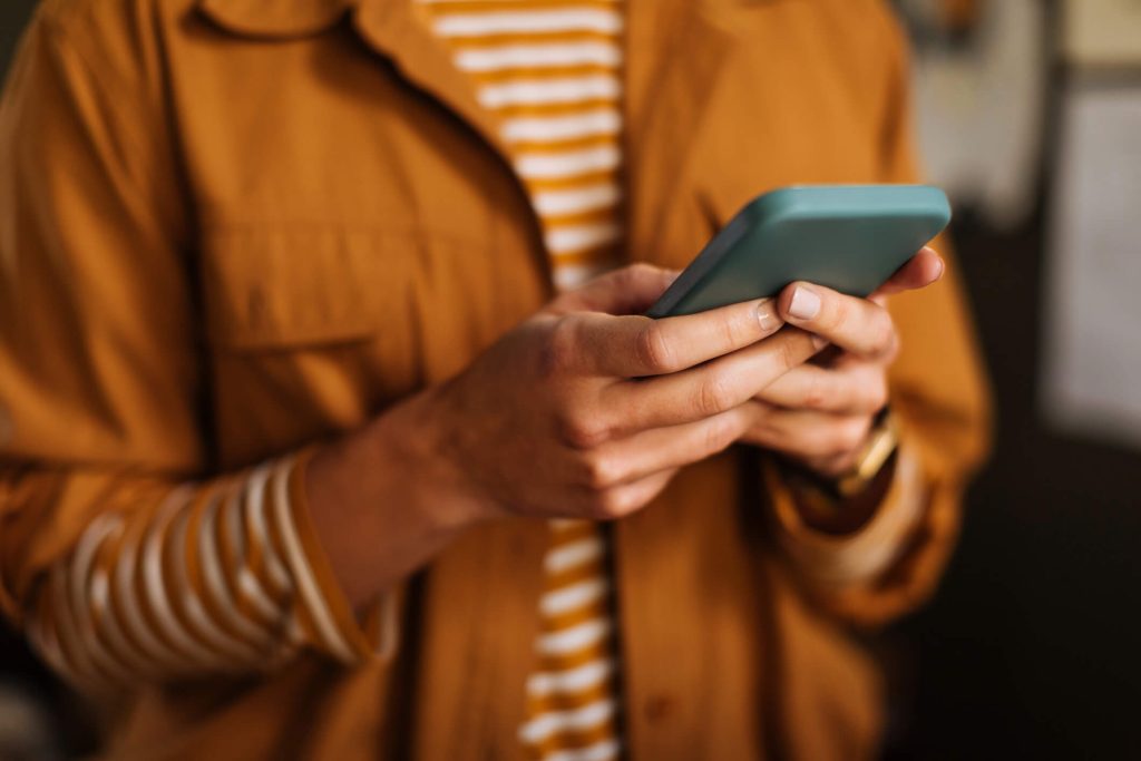 Mãos seguram um celular e digitam algo nele, de forma que não é possível o que é.