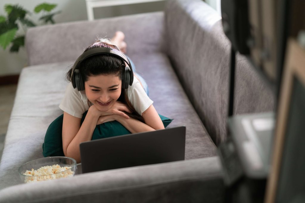 Mulher sorridente assistindo em stremaing no laptop no sofá na sala de estar em casa.