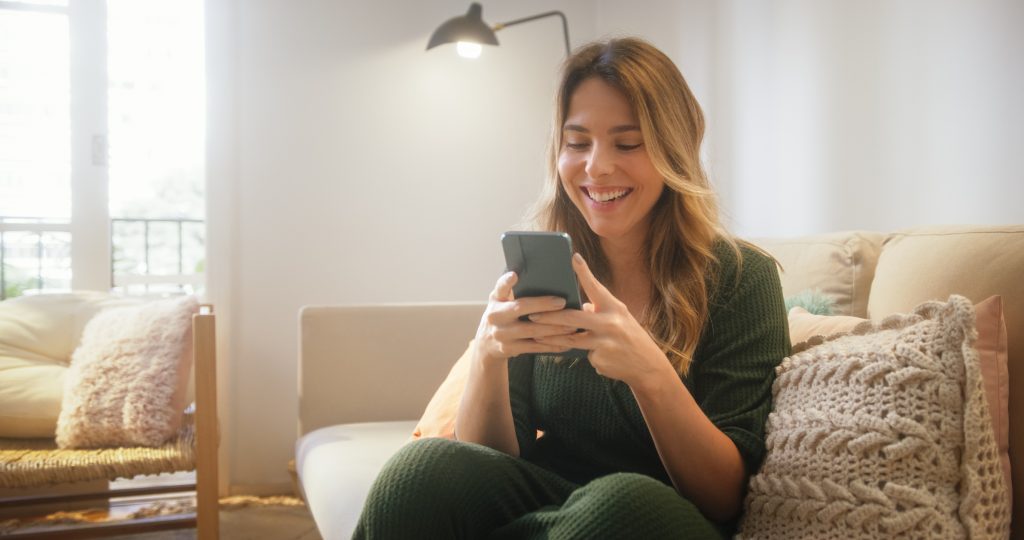 Bela mulher caucasiana usando smartphone na sala de estar.