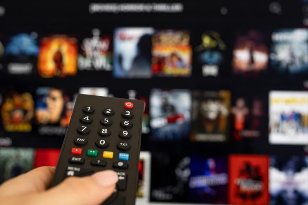 Mão da mulher segurando o controle remoto da TV.