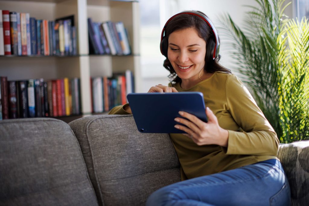 Mulher sorridente relaxando com tablet digital no sofá em casa.