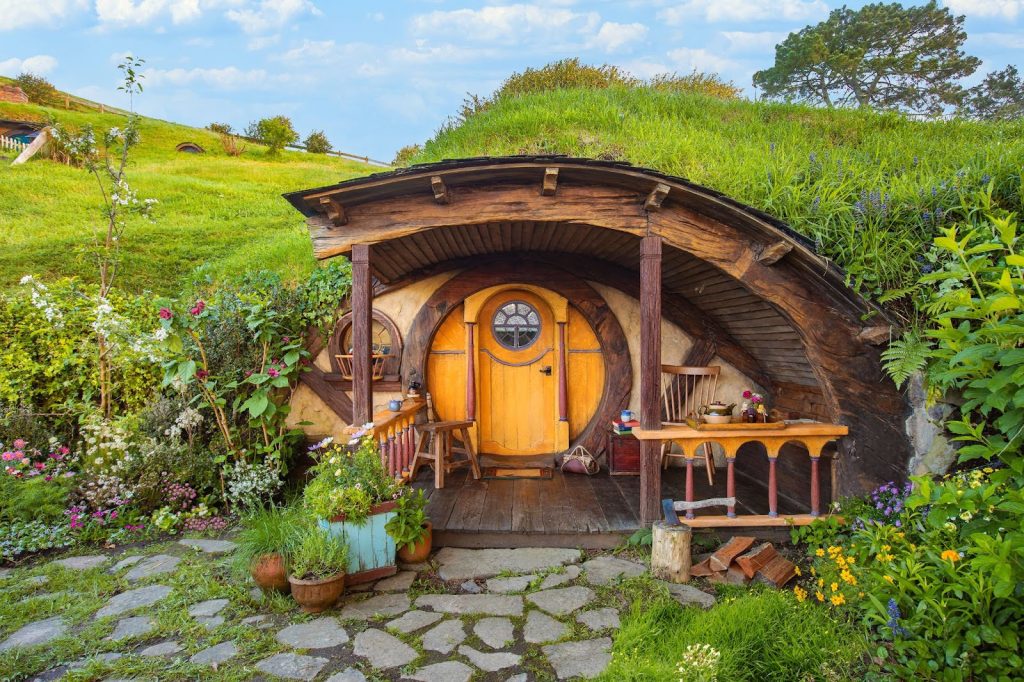 Cabana rústica de madeira com flores na portal e construída no formato oval.