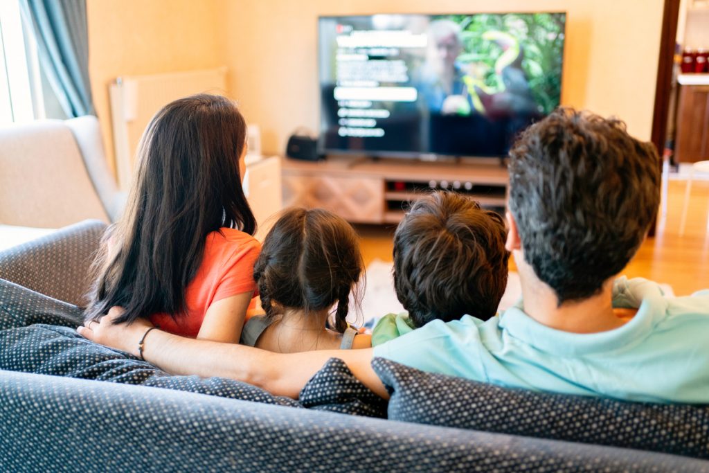 Pais e seus dois filhos assistindo TV juntos em casa.