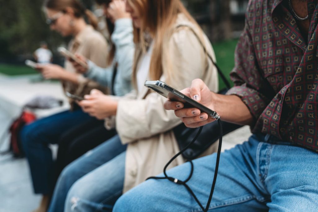 Quatro amigos estão usando telefones inteligentes enquanto estão sentados em um parque público na cidade.