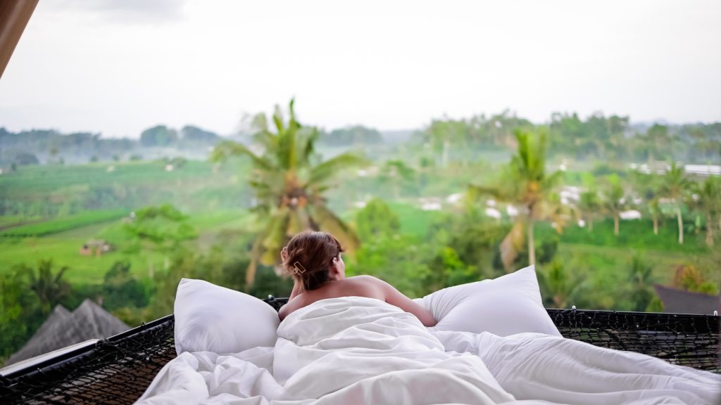Mulher relaxando em um cama com lençóis brancos.