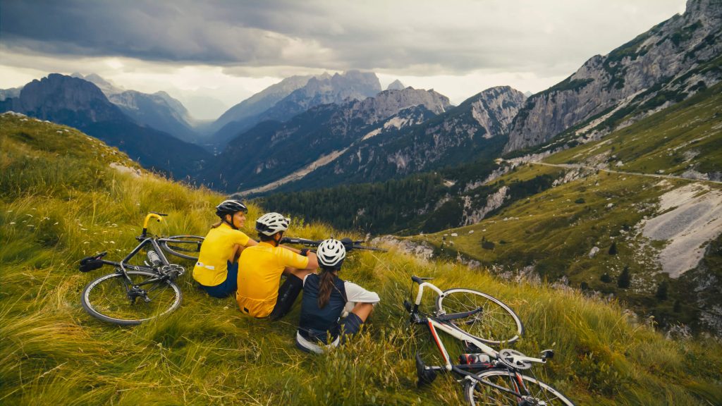 Ciclistas adultos de meia idade relaxam em uma parte superior de uma montanha com vista cénica do vale.