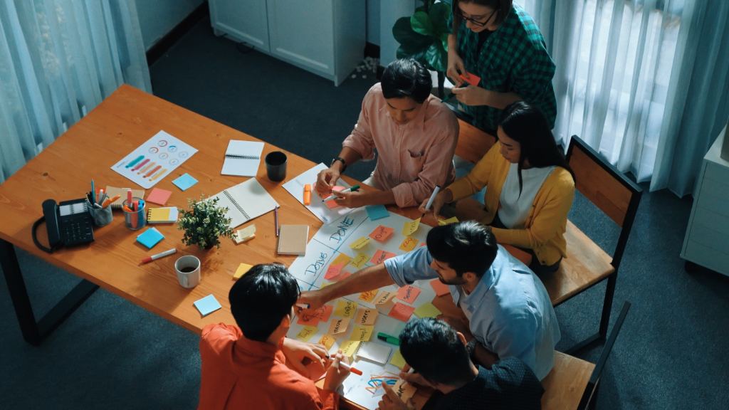 Vista aérea de uma equipe de profissionais de marketing reunida em torno de uma mesa com post-its e gráficos, planejando estratégias de posicionamento de mercado e analisando tendências do consumo de álcool no Brasil.