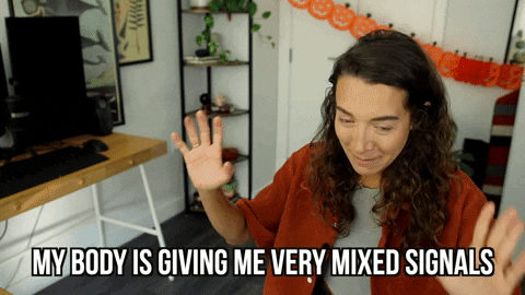 GIF de uma mulher com expressão confusa e mãos levantadas, gesticulando incerteza. Abaixo, a legenda em inglês diz: "My body is giving me very mixed signals" (Meu corpo está me enviando sinais muito confusos). O ambiente ao fundo é um escritório doméstico.