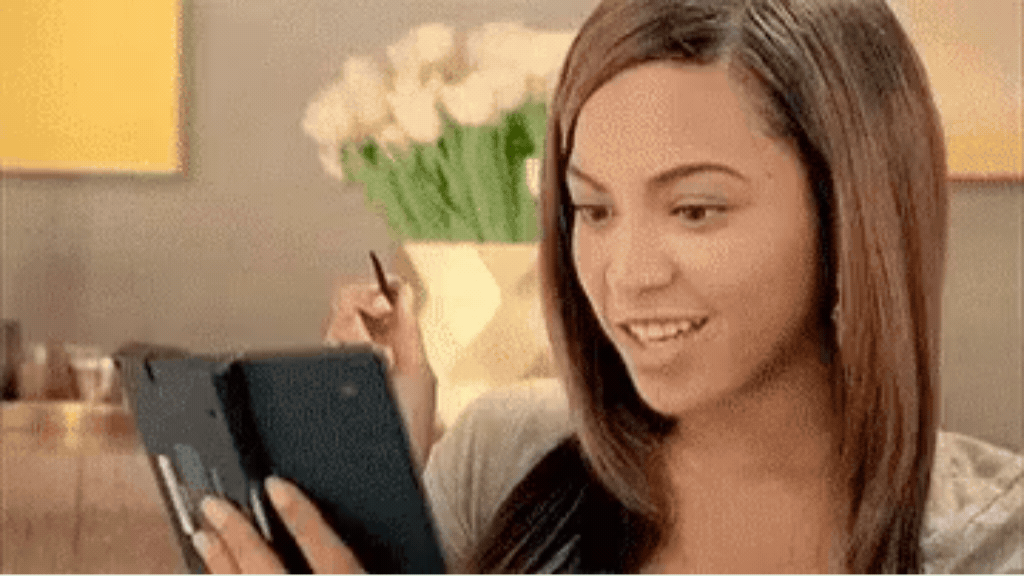 A cantora Beyoncé sorrindo entusiasmada enquanto mexe em um dispositivo portátil, representando a descoberta visual de novos produtos e conteúdos pelas gerações.