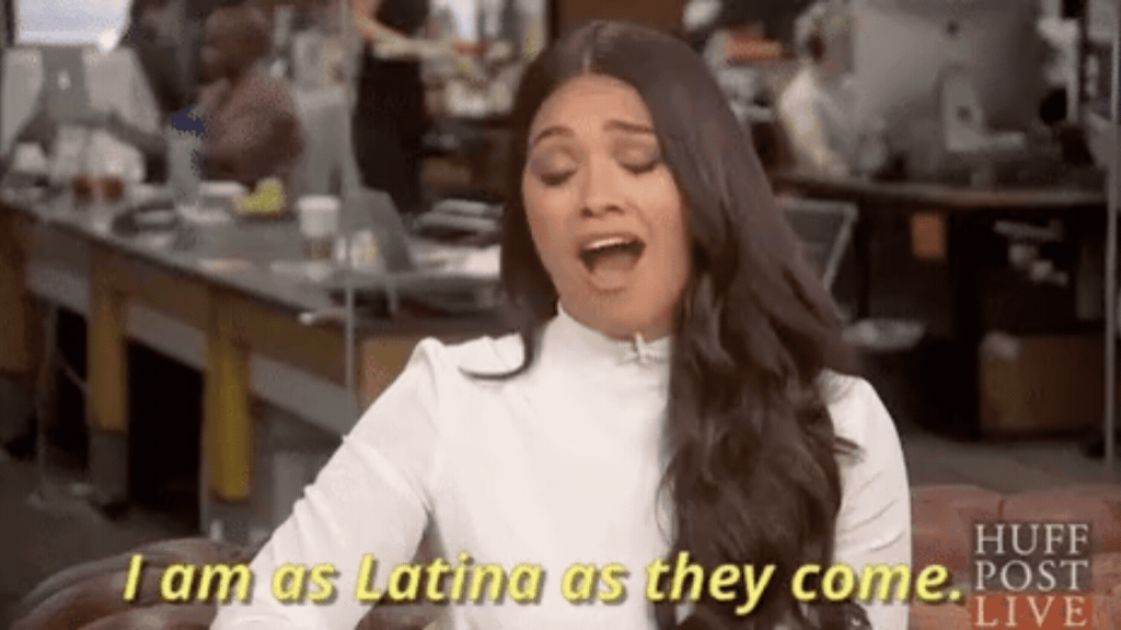 Uma captura de tela de uma entrevista em vídeo, mostrando uma mulher com longos cabelos escuros e blusa branca, com uma expressão animada e a boca aberta. Na parte inferior da imagem, há legendas em inglês que dizem "I am as Latina as they come", representando a américa latina.