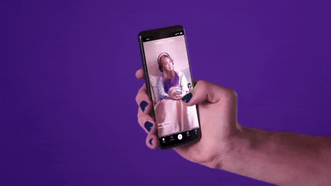 GIF em fundo roxo com uma mão segurando um smartphone na vertical e deslizando a tela (feed de vídeos), representando o consumo contínuo e o crescimento dos aplicativos de microdrama.