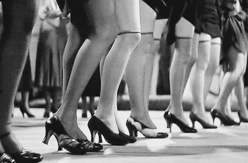 GIF em preto e branco de pernas de dançarinas vintage em movimento usando sapatos de salto alto, ilustrando a teoria do High Heel Index e a saturação de mídia.